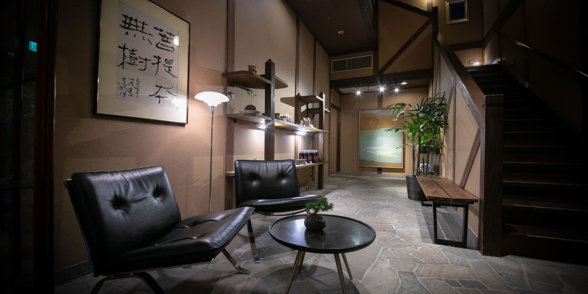 Lobby lounge with leather chairs, stone floor and calligraphy artwork inside Yufuin Bettei Kazenomori