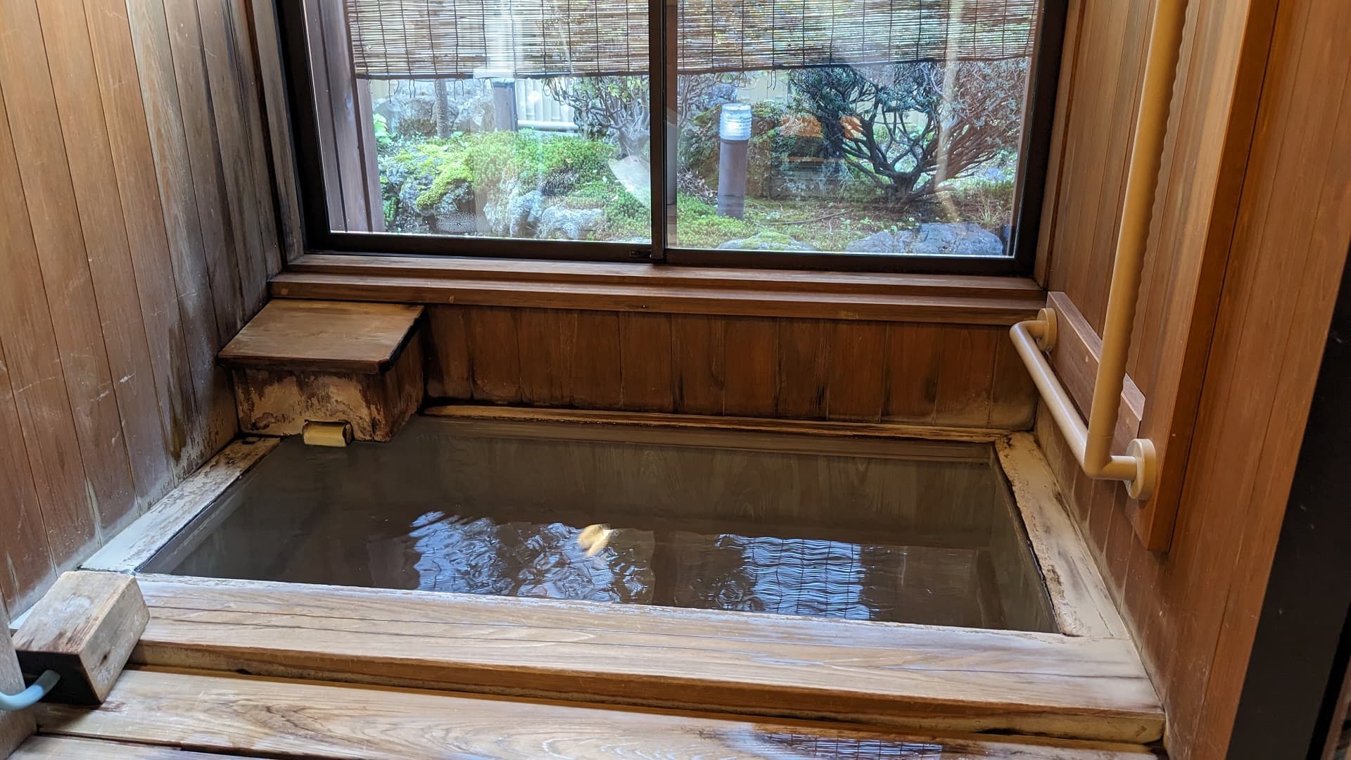 Private in-room Shirahata-source hot-spring bath at Ekinariya Ryokan with a garden view through the window