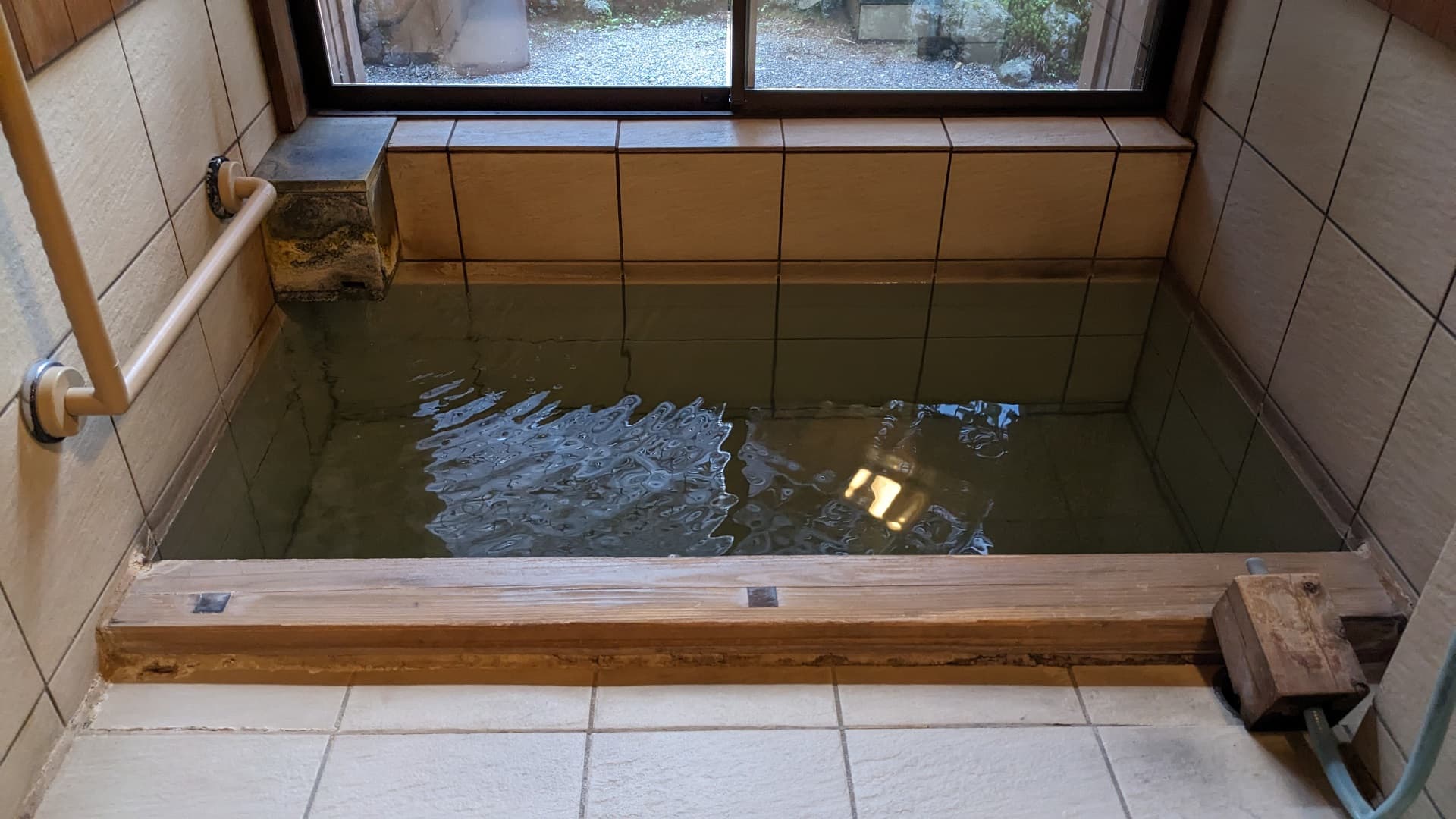 Private tiled Yubatake-source hot-spring bath at Ekinariya Ryokan beside a window overlooking the grounds