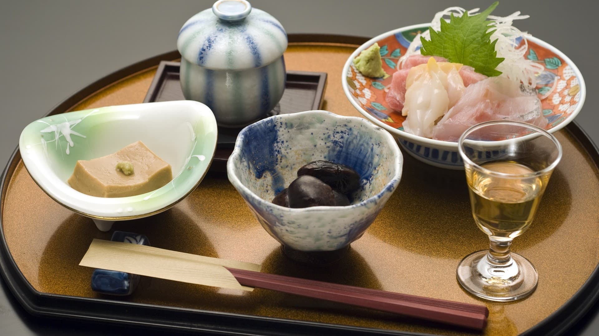 Kaiseki appetizer tray at Ekinariya Ryokan with sashimi, sesame tofu, a simmered dish and a glass of sake