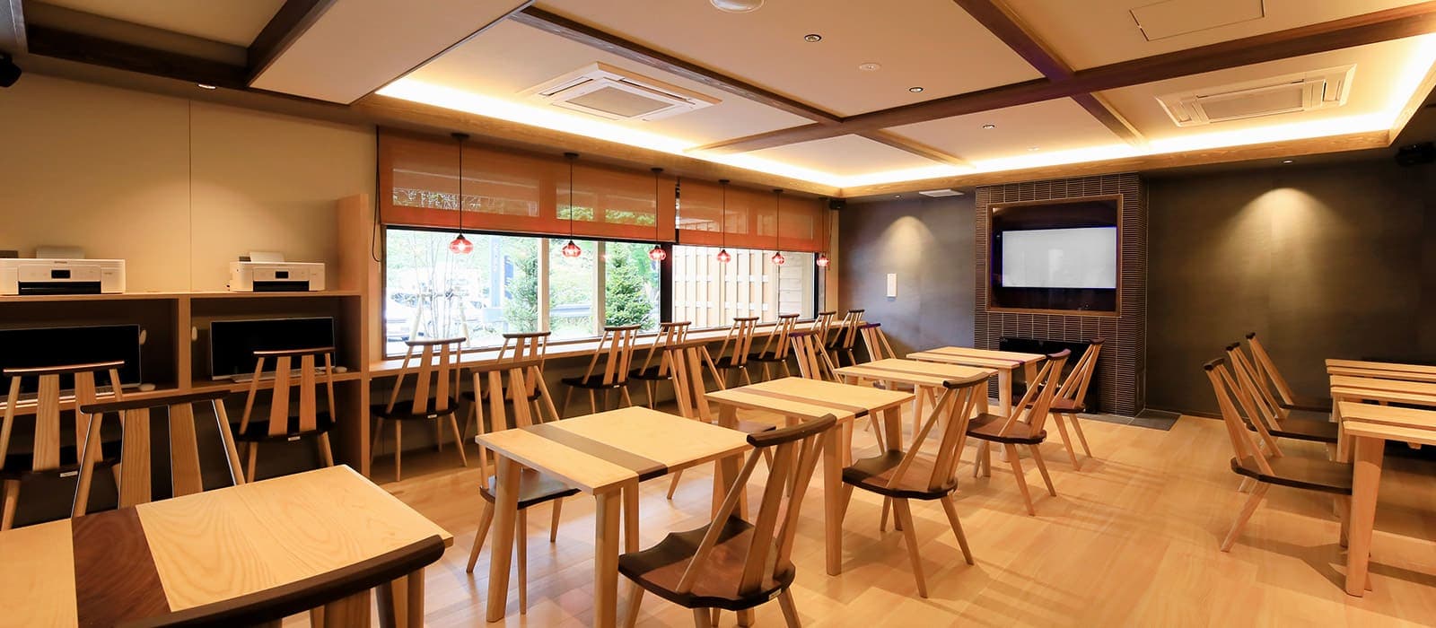 Bright dining lounge with light wood tables and chairs and a garden-facing window