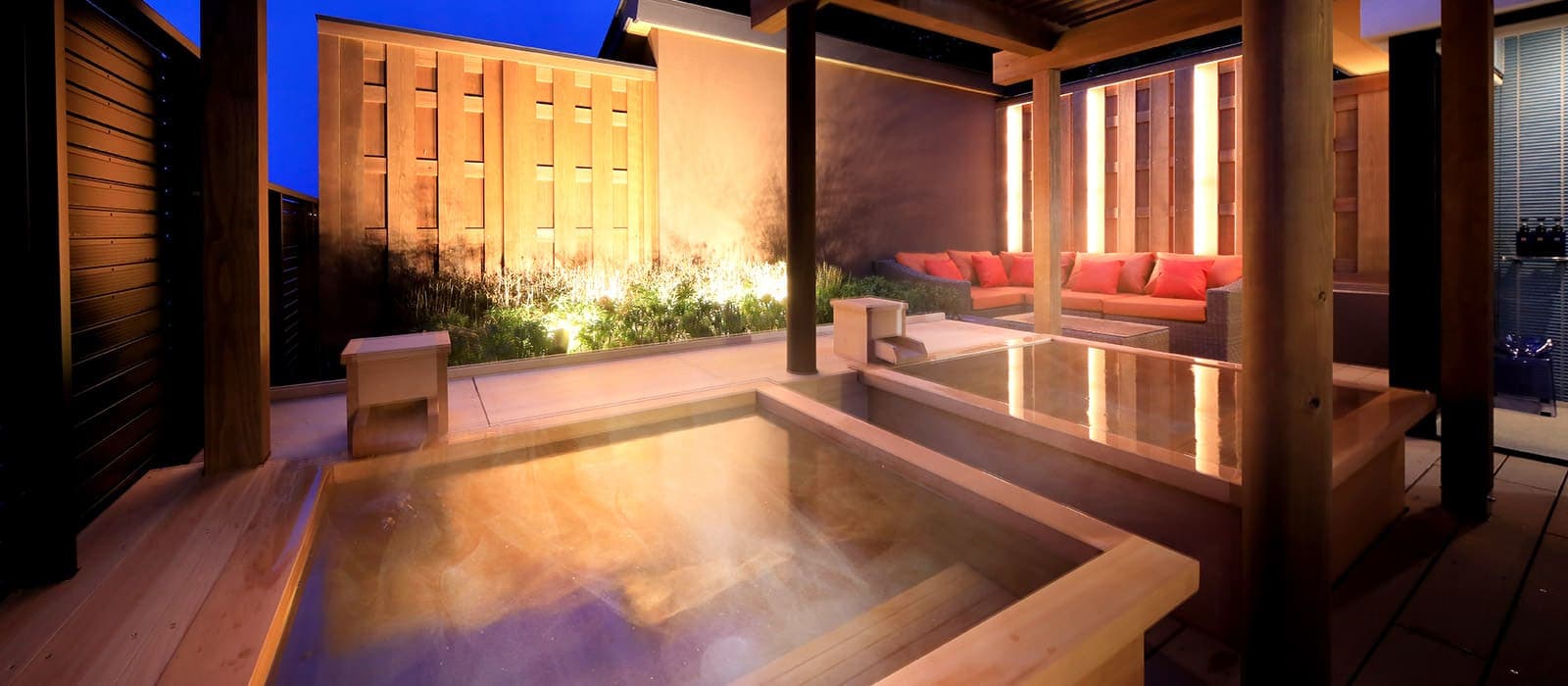 Private open-air cypress rotenburo bath at dusk with garden lighting and lounge seating