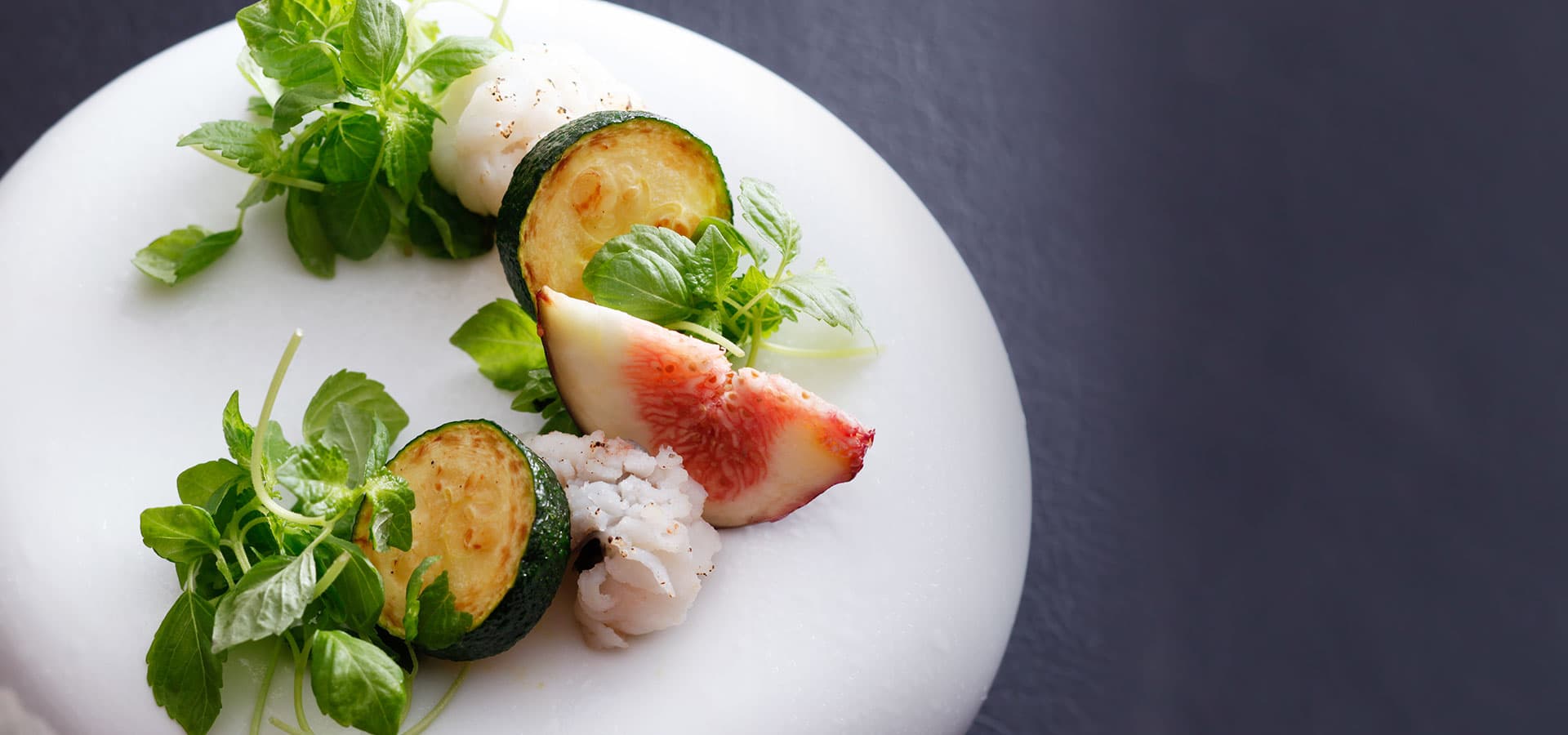 Plated kaiseki appetizer detail at Miyukiso Hanamusubi with fig, zucchini and herbs on a white ceramic dish