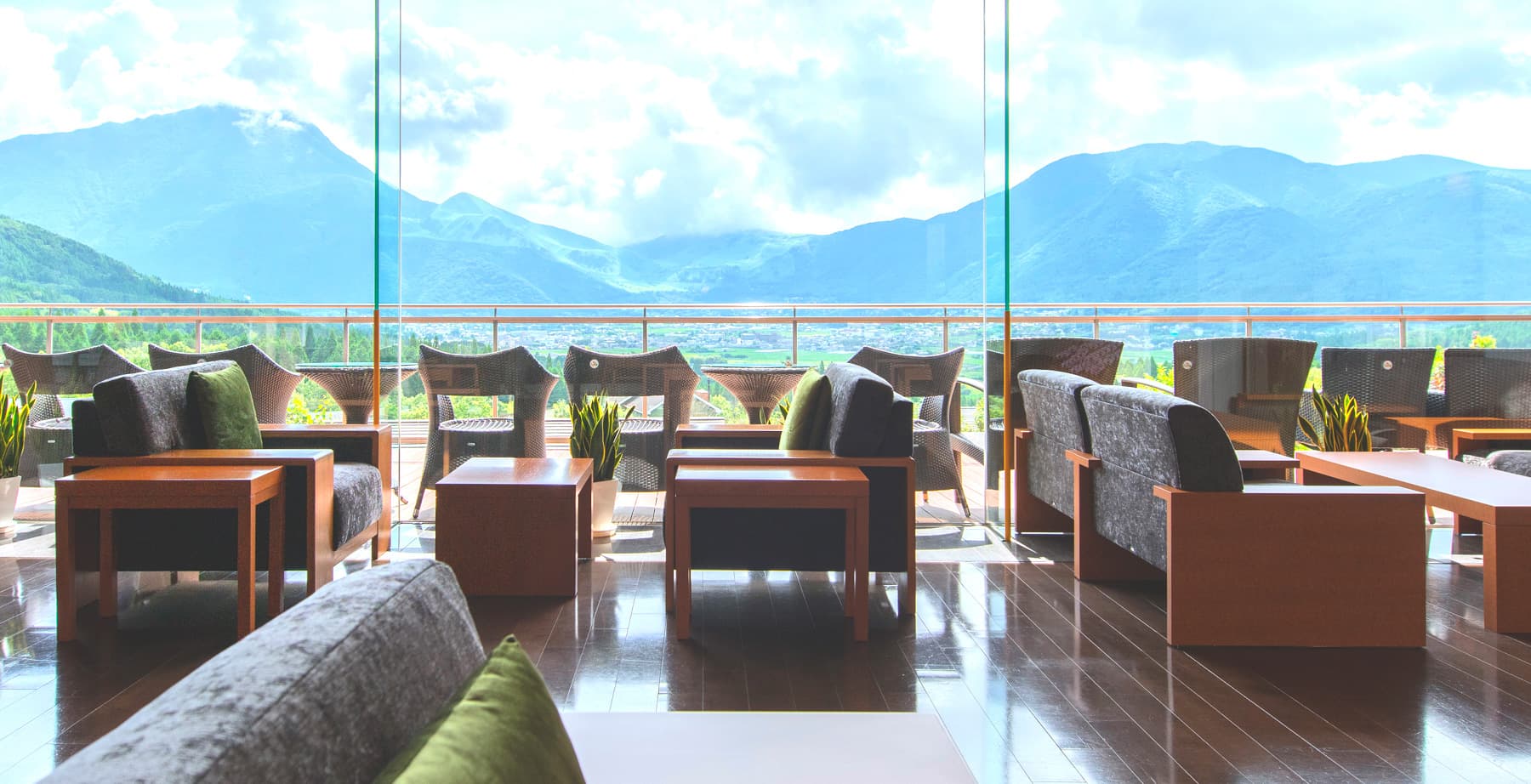 Lounge at Yufuin Hanayoshi with sofa seating and floor-to-ceiling windows opening to a Mount Yufu panorama