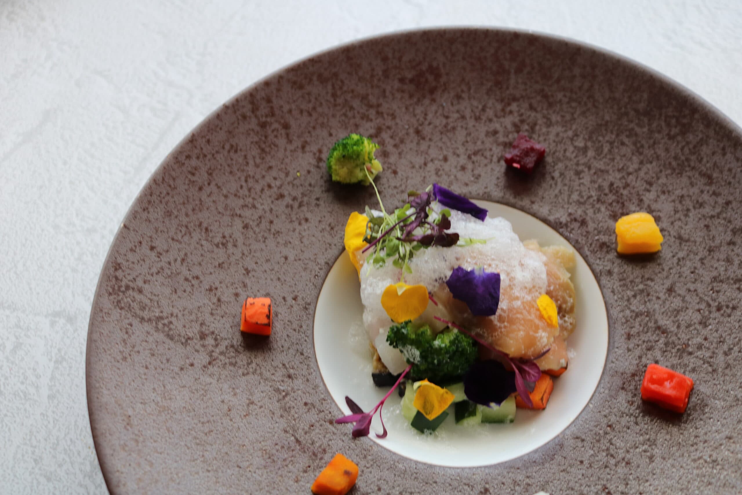 Plated kaiseki course at Hotel Village with white fish, vegetables and edible flowers on a stone-glazed plate