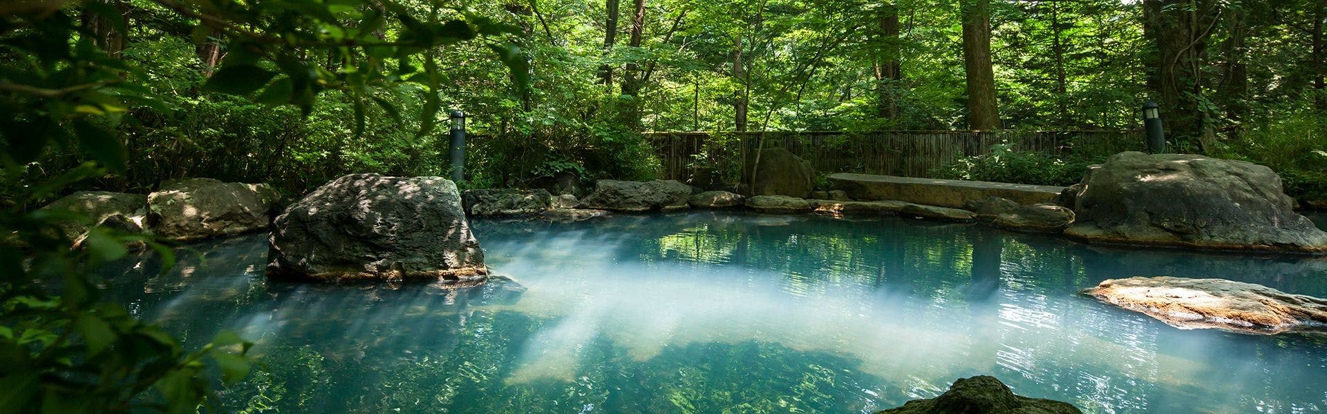 Outdoor rock onsen bath surrounded by lush green forest