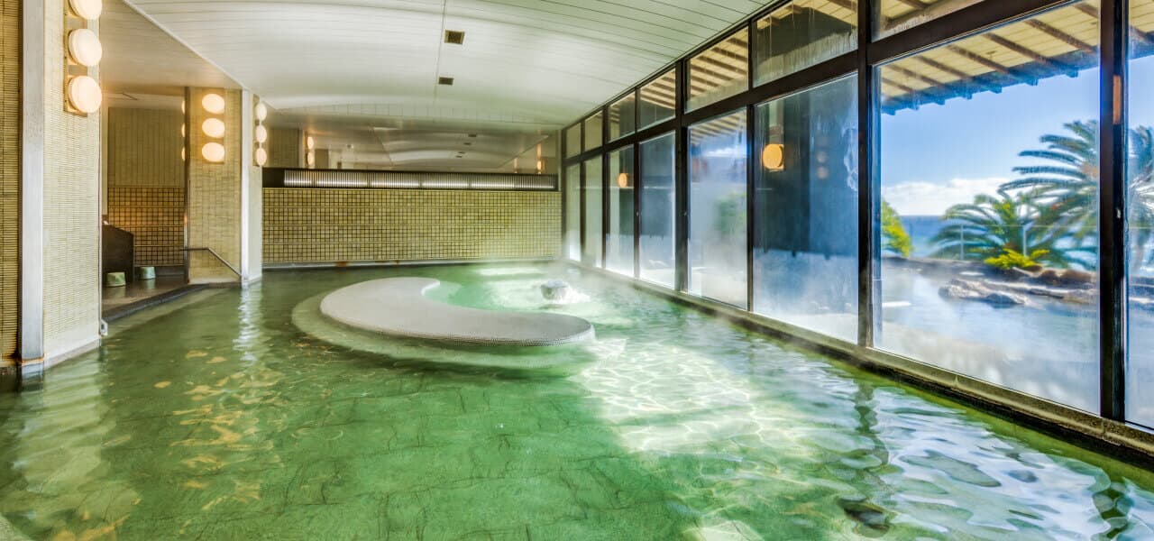 Indoor onsen bath with floor-to-ceiling windows and sea view at Inatori Ginsuiso, Inatori Onsen