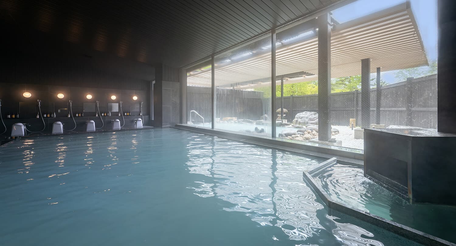 Spacious indoor large bath with washing stations and floor-to-ceiling windows facing the rock garden