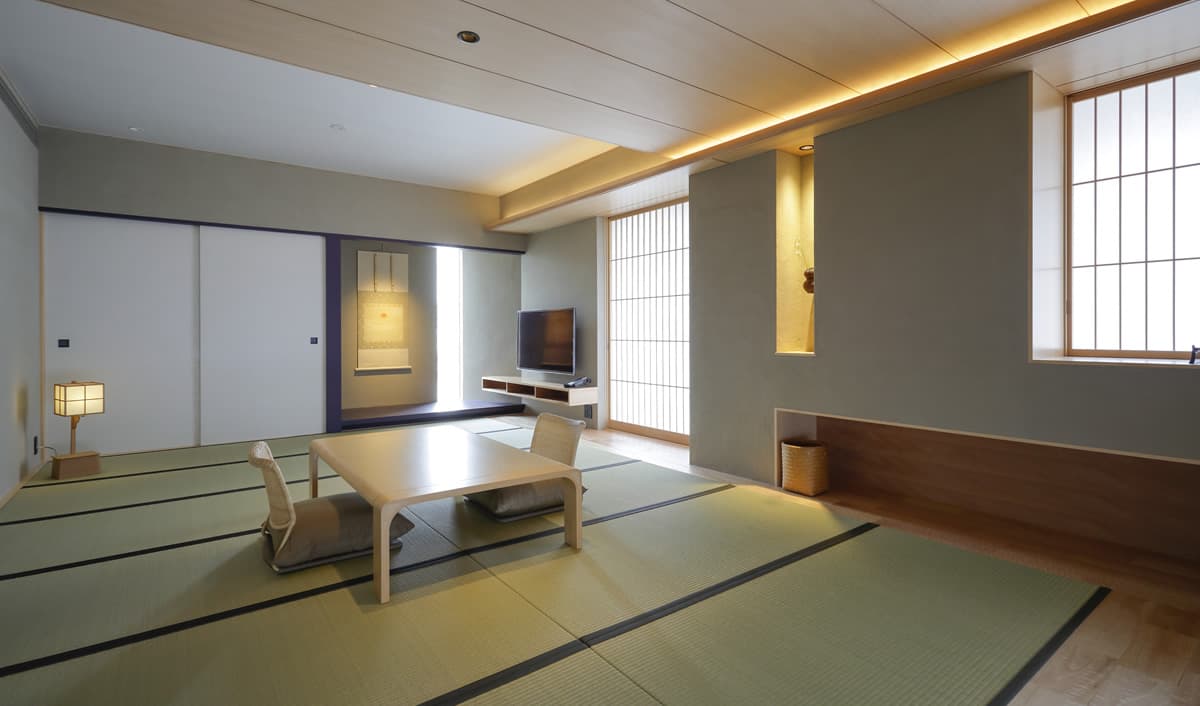 Spacious modern tatami guest room with low table, floor chairs, hanging scroll and shoji-screened windows at Kaminarimon Ryokan
