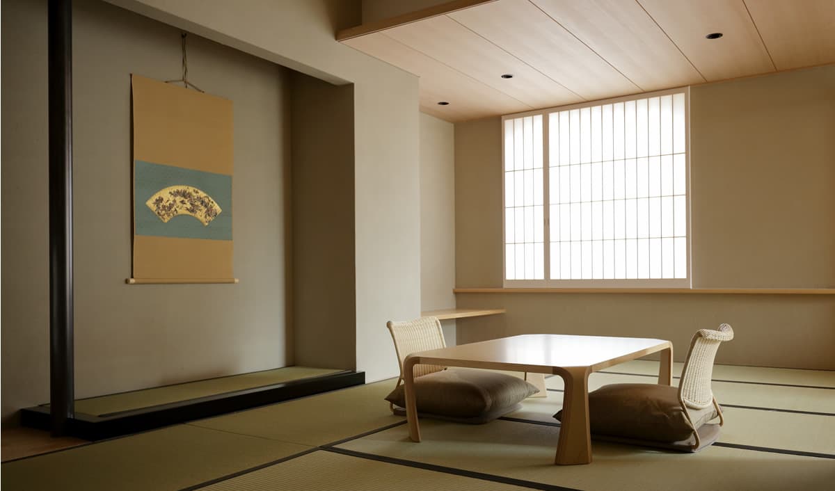 Minimalist Japanese-style room with a fan-painting hanging scroll, low wooden table and tatami flooring at Kaminarimon Ryokan in Asakusa