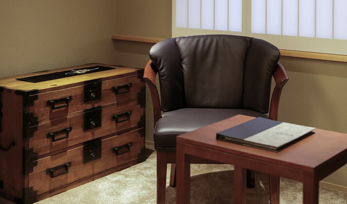 Detail of a leather armchair, antique wooden tansu chest and side table in a guest room at Kaminarimon Ryokan, Asakusa Tokyo