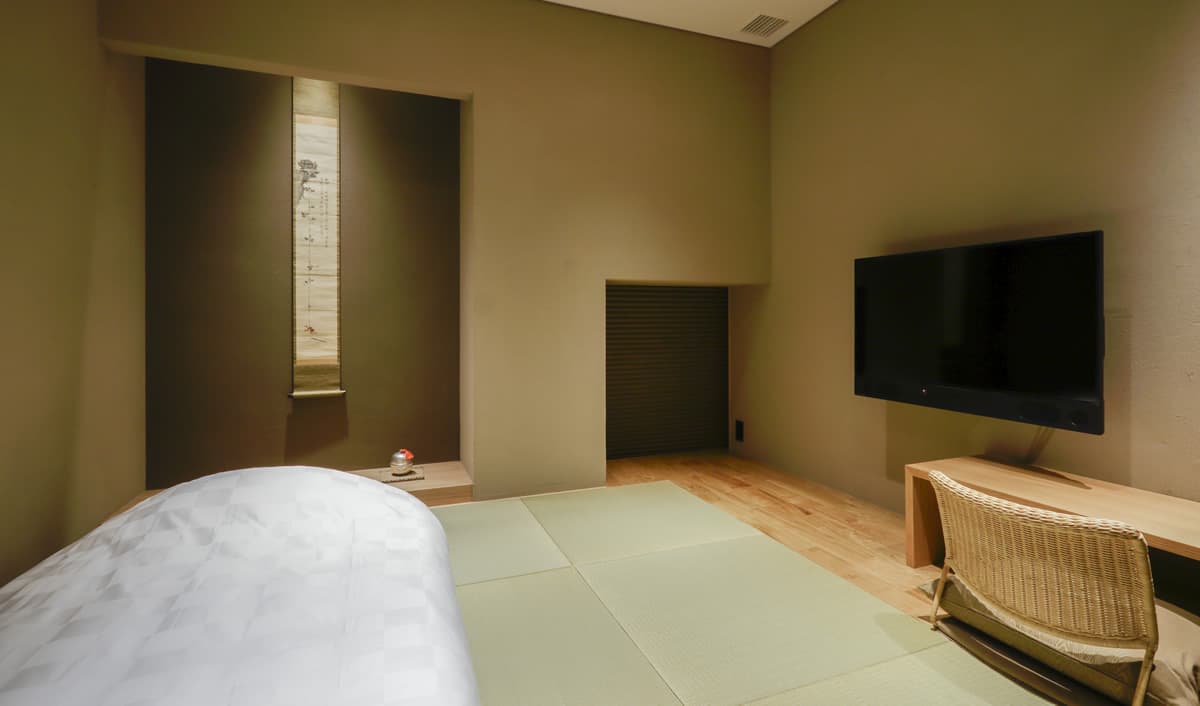 Calm tatami room with white bedding, a vertical hanging scroll and wall-mounted TV at Kaminarimon Ryokan in Asakusa