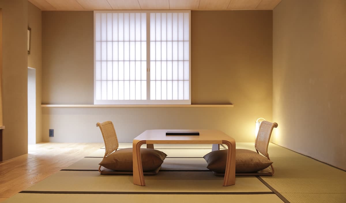 Bright tatami guest room with low table, woven floor chairs and a large shoji-filtered window at Kaminarimon Ryokan, Asakusa