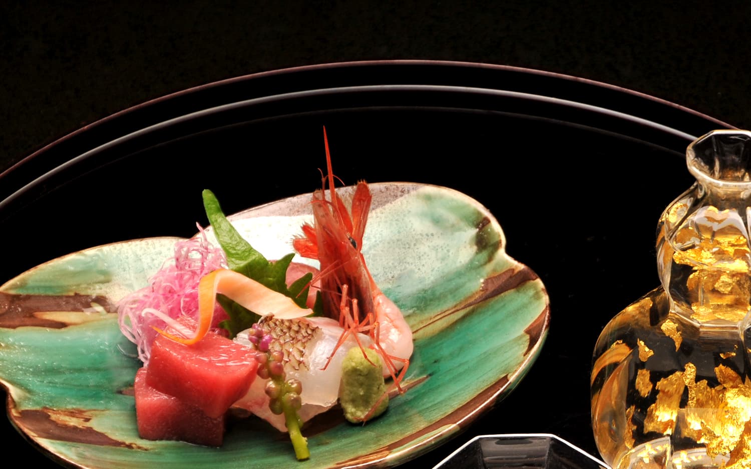 Kaiseki sashimi course at Kankaso ryokan in Nara, fresh tuna, prawn and white fish arranged on a green glazed plate with gold-flecked sake