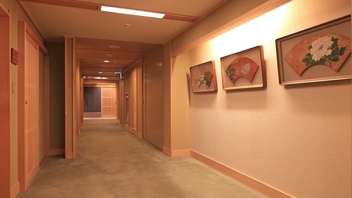 Warmly lit interior corridor with wood detailing and framed Japanese fan artwork at Kasuga Hotel
