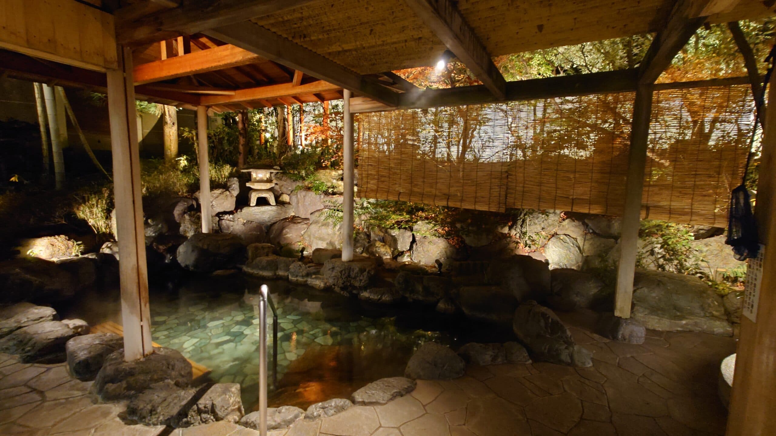 Steaming open-air rotenburo bath lit by lanterns among rocks and trees in the evening at Kasuga Hotel