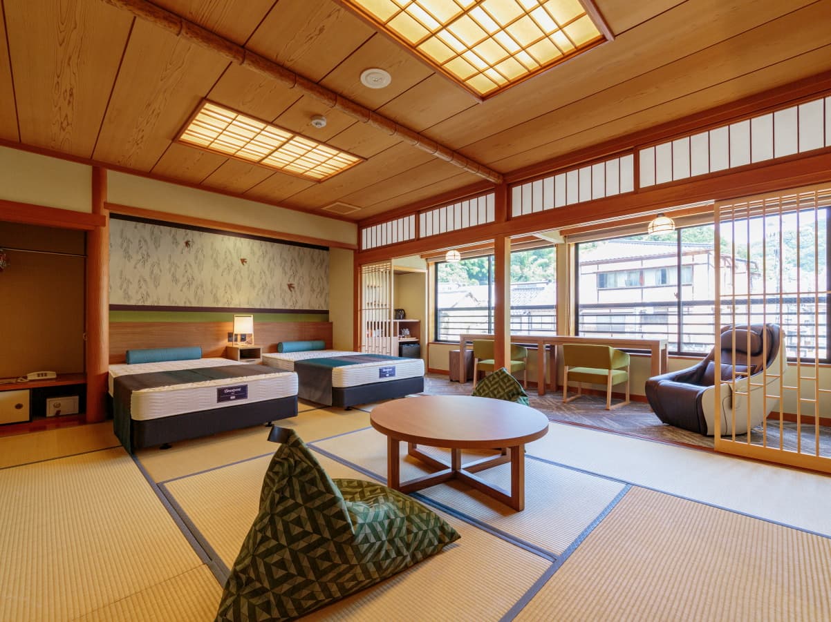 Tatami guest room with twin beds, low table and massage chair facing garden windows, Kawaguchiya Honkan, Kinosaki Onsen