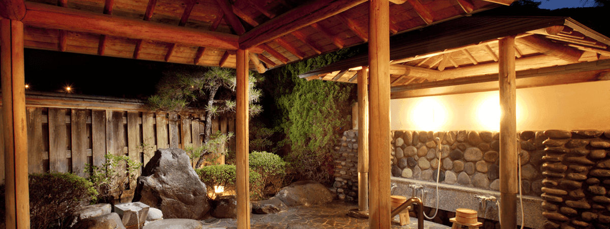 Covered private rotenburo with timber pillars and stacked-log wall in a lantern-lit courtyard, Kawakamiya Kasuitei, Gero Onsen