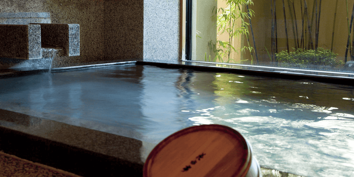 Granite indoor hot-spring bath with steaming water and a wooden ladle by the garden window, Kawakamiya Kasuitei, Gero Onsen