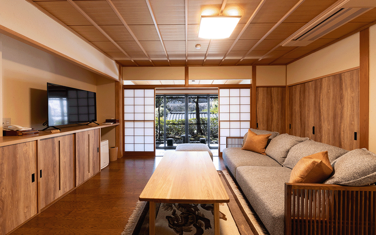 Spacious tatami living room with low table and long sofa opening onto a green garden, Kawakamiya Kasuitei, Gero Onsen