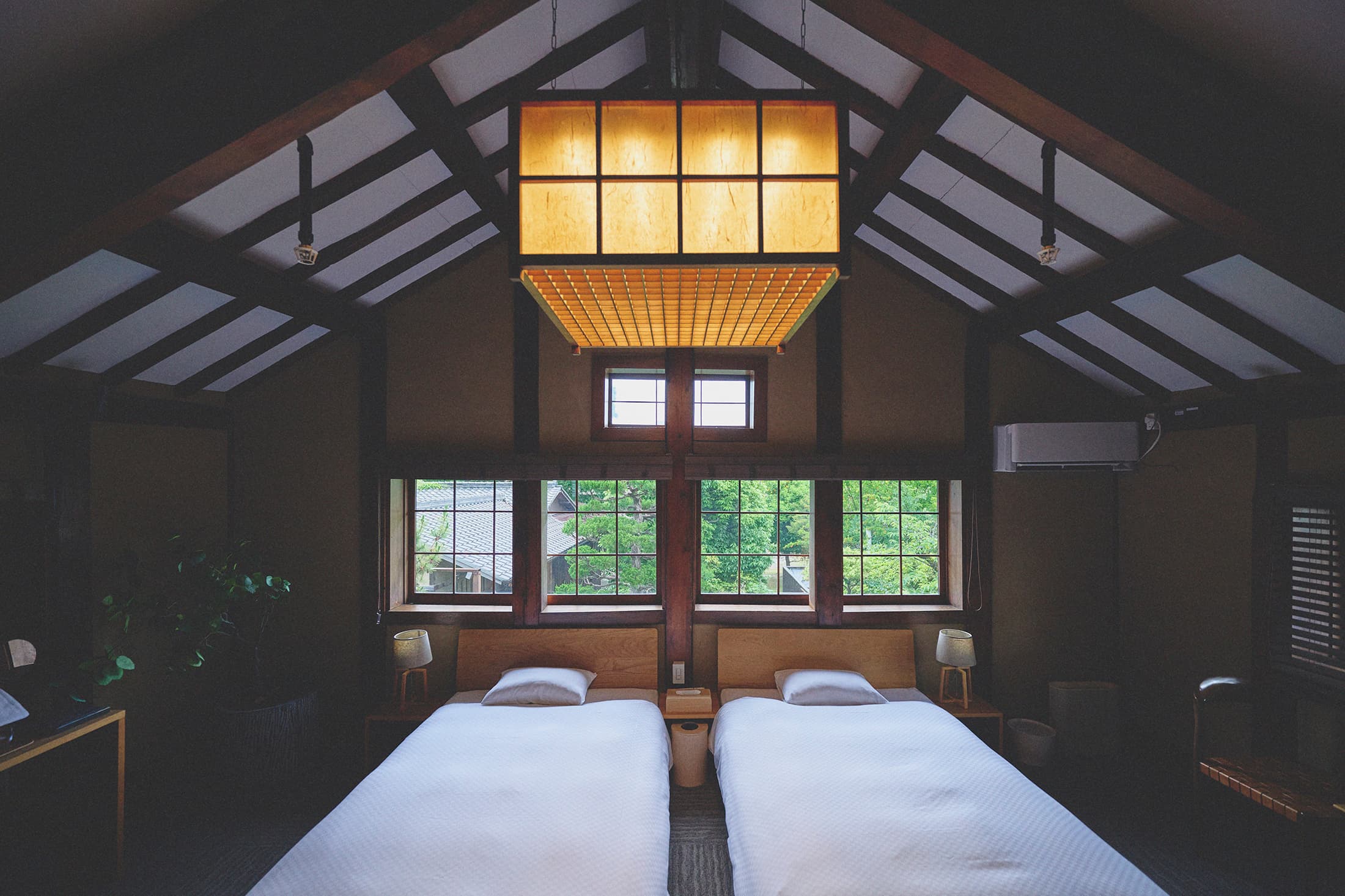 Machiya guest room at Kaze no Naramachi with twin beds beneath an exposed timber gable and a glowing paper lantern