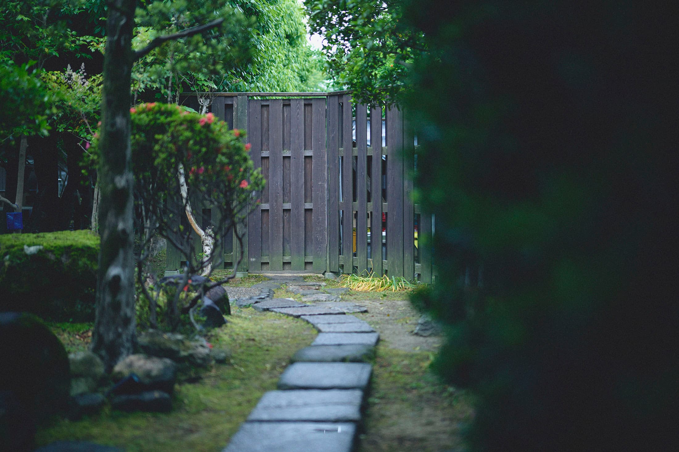 Stone-paved path winding through the green inner garden of Kaze no Naramachi toward a wooden gate