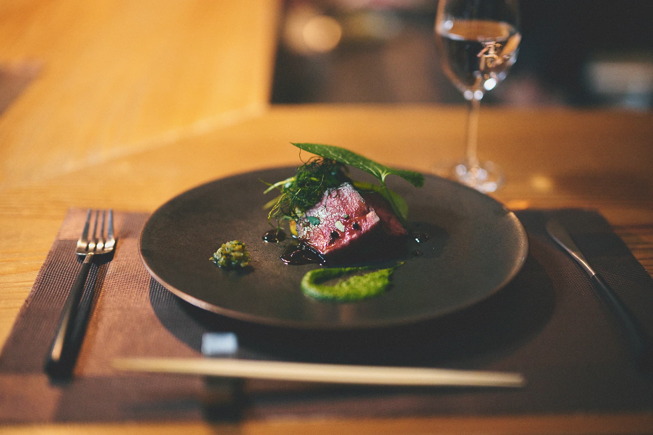Plated wagyu beef course with herbs and dark sauce on a charcoal plate at Kaze no Naramachi's dining counter