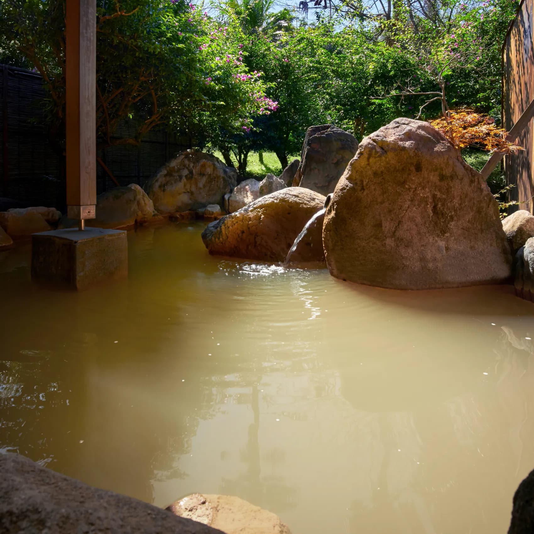 Outdoor rotenburo with golden mineral beauty-onsen water and garden rocks at Koran no Yu Kinkouroh in Ibusuki