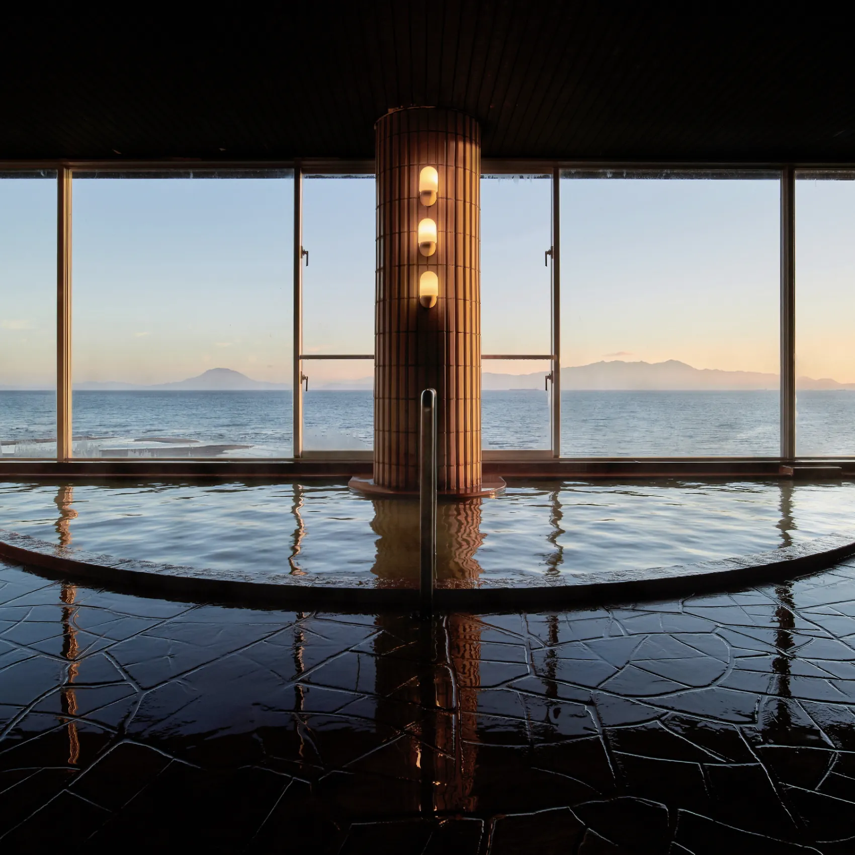 Indoor onsen bath with panoramic ocean view across Kinko Bay at sunrise at Koran no Yu Kinkouroh in Ibusuki