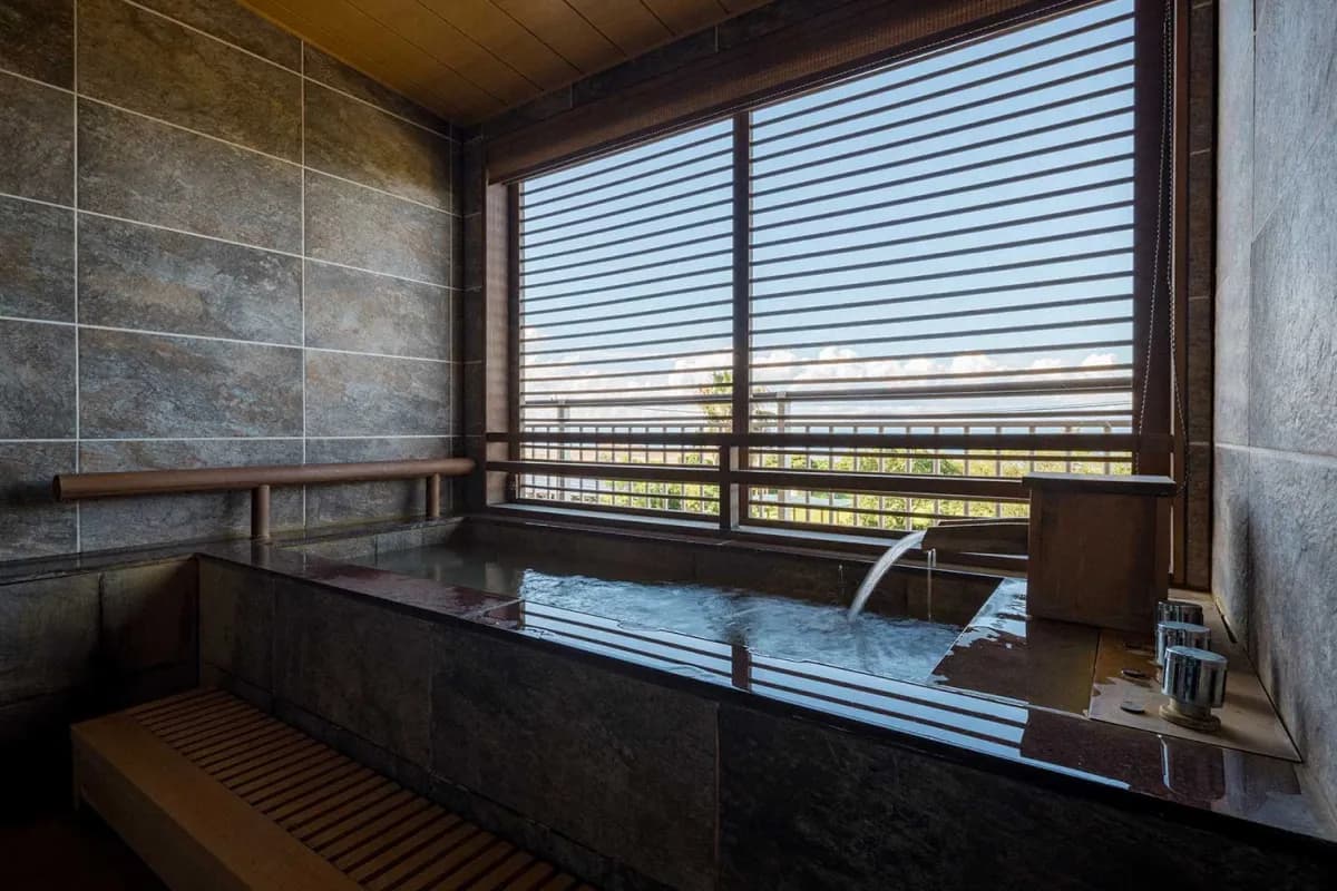 Private in-room stone bath with a slatted view window at Koran no Yu Kinkouroh in Ibusuki