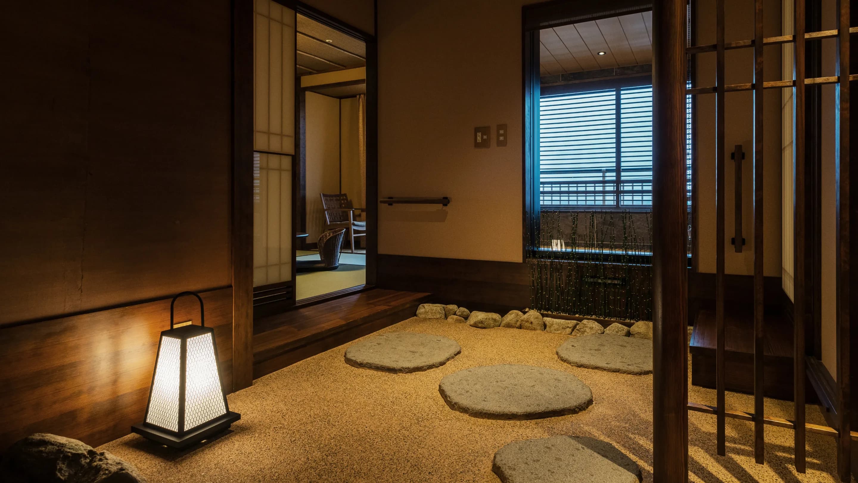 Guest room interior with a paper lantern, raked-gravel zen entry and bay-view window at Koran no Yu Kinkouroh