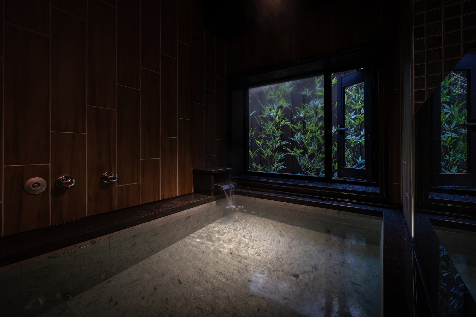 Private reservable stone bath at Kinsuikan with dark wood walls and a bamboo garden window