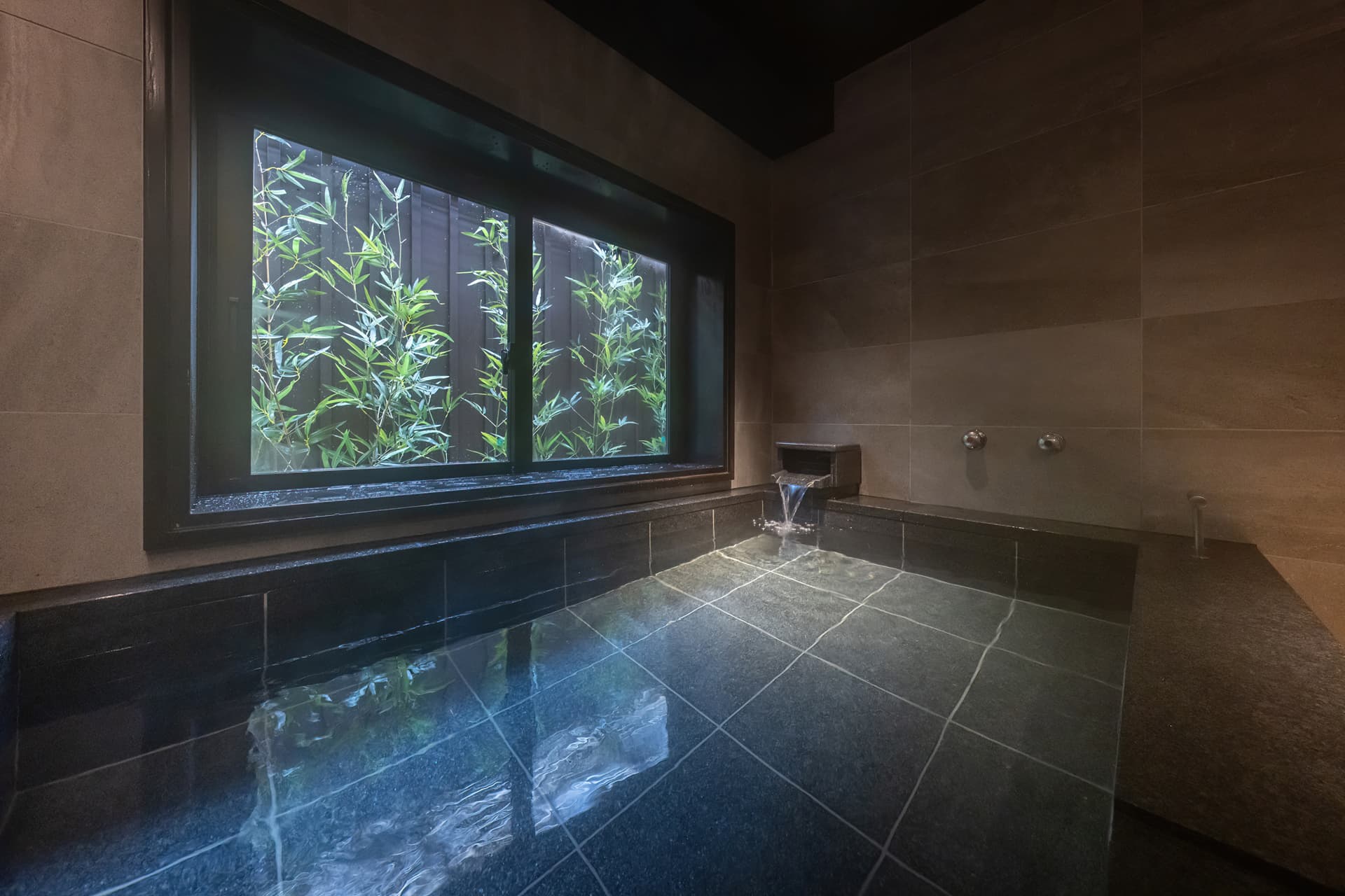 Private reservable bath at Kinsuikan in dark stone with steaming water and a bamboo garden view