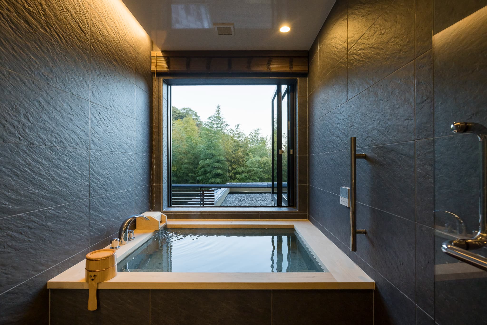 In-room private bath at Kinzan with a sunken tub of dark stone tile opening through a window to a green bamboo garden