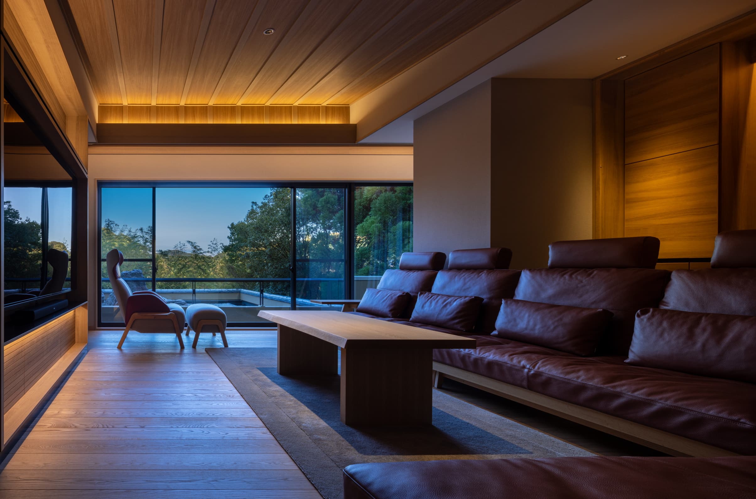 Guest room lounge at Kinzan at dusk with leather sofas, wood ceiling and floor-to-ceiling windows over the valley