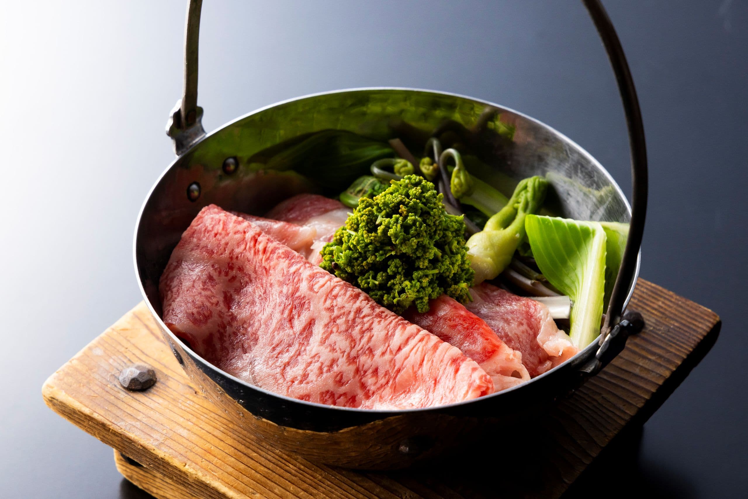 Marbled wagyu beef sukiyaki hot pot simmering in an iron pan over a wooden stand at Kinzan