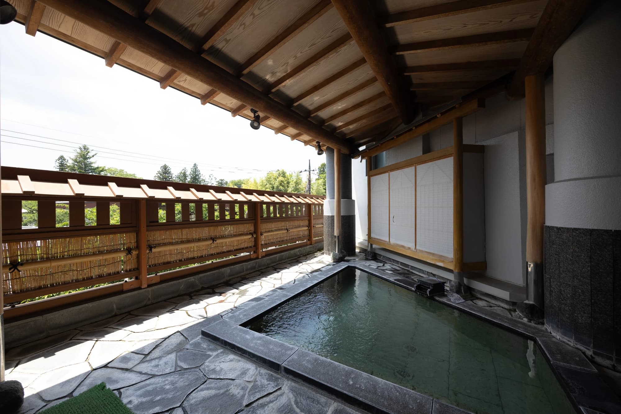 Outdoor rotenburo bath at Konansou with a stone tub under a wooden roof beside a bamboo fence and garden
