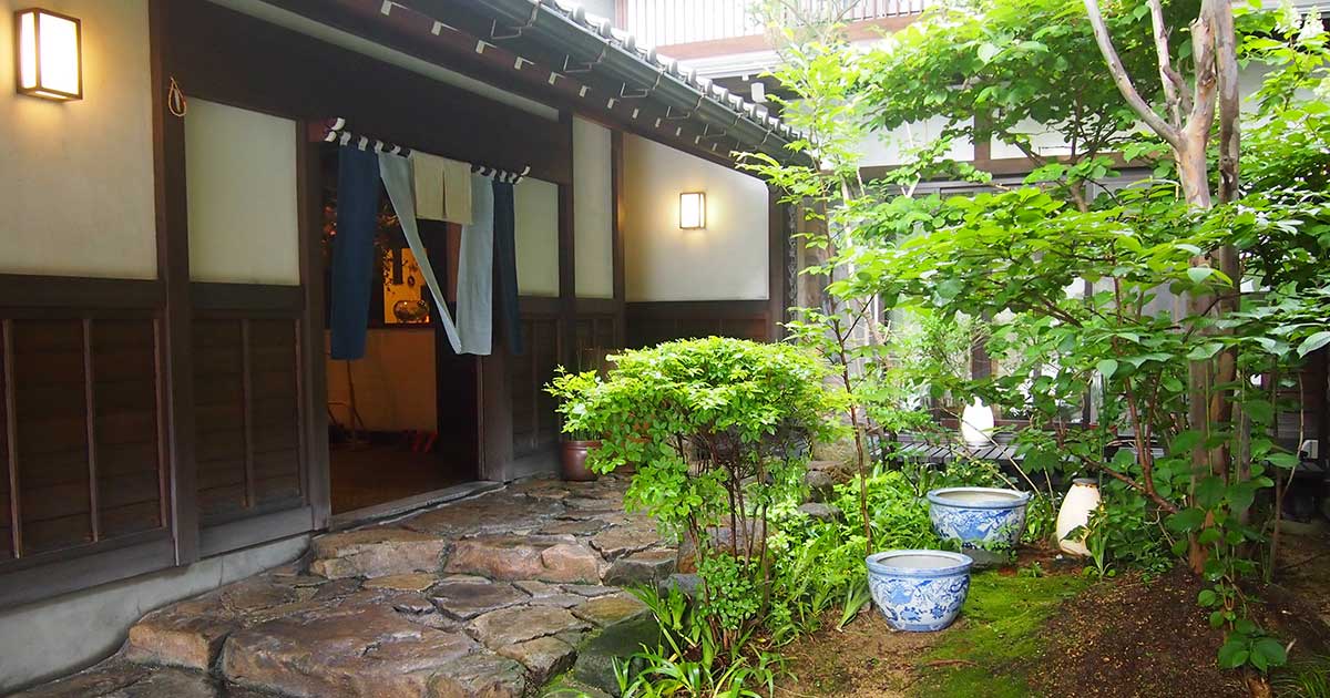 Stone-paved entrance and inner garden of Oyado Koto no Yume ryokan in Takayama, with indigo noren curtain and lantern
