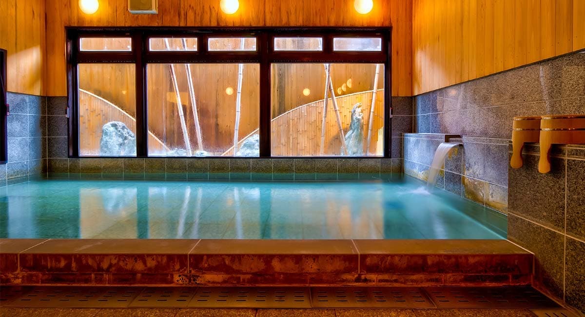 Spacious indoor hot spring bath at Oyado Koto no Yume, Takayama, with stone tiling and bamboo garden view through wide windows