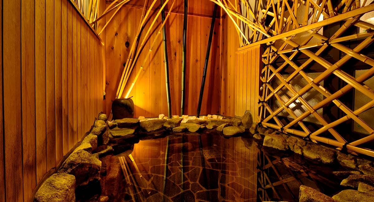 Atmospheric rock-edged indoor onsen bath framed by bamboo and lattice screens at Oyado Koto no Yume in Takayama