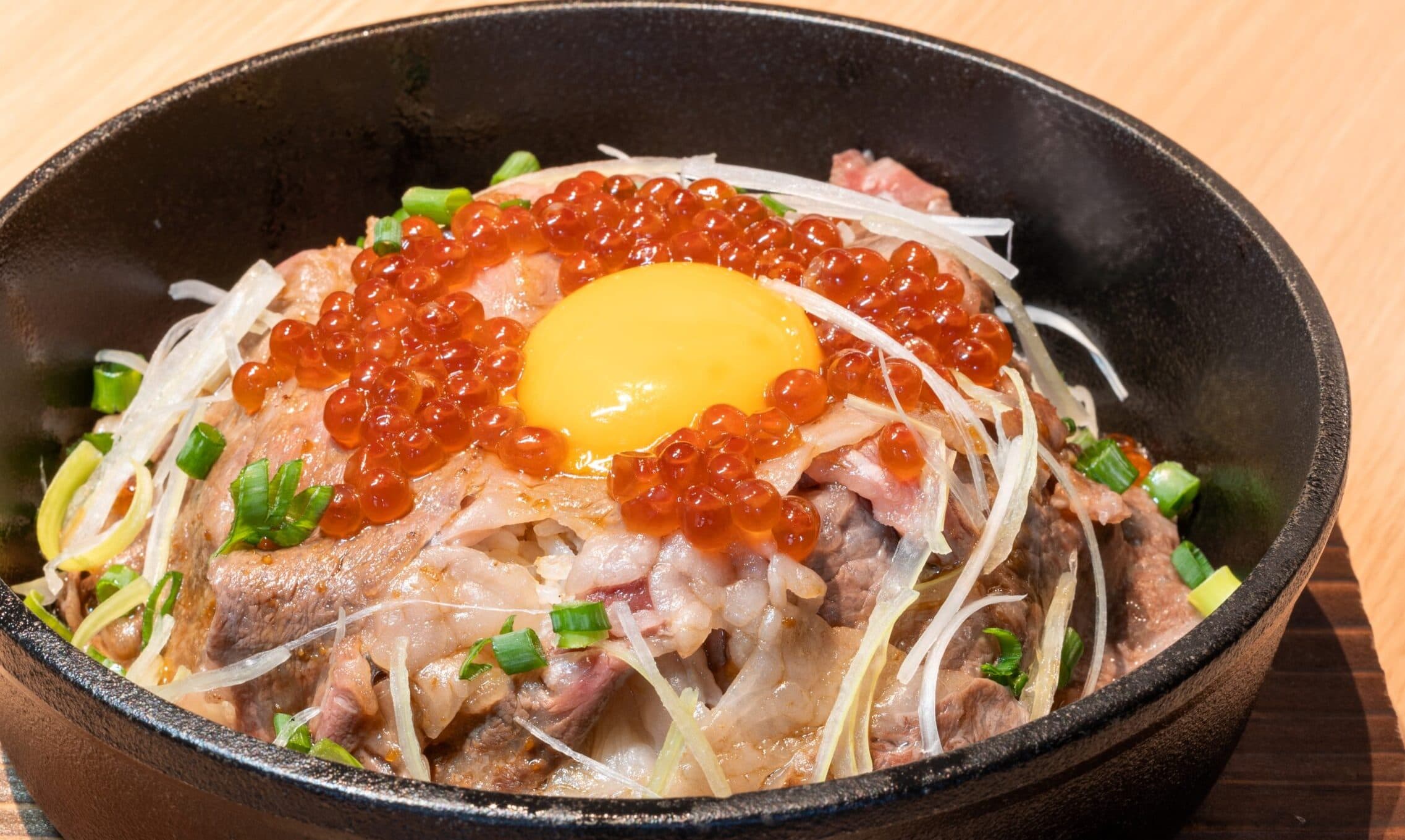 Yubatake Sensui signature beef-and-salmon-roe rice bowl topped with a raw egg yolk, ikura, shredded leek and herbs in a cast-iron pan