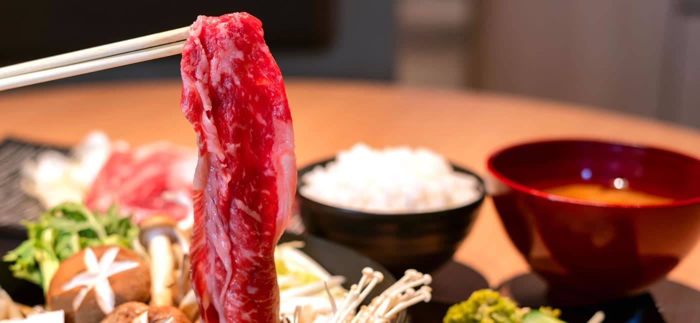 Yubatake Sensui dinner, a slice of marbled wagyu beef lifted with chopsticks over a sukiyaki pot with rice and miso soup
