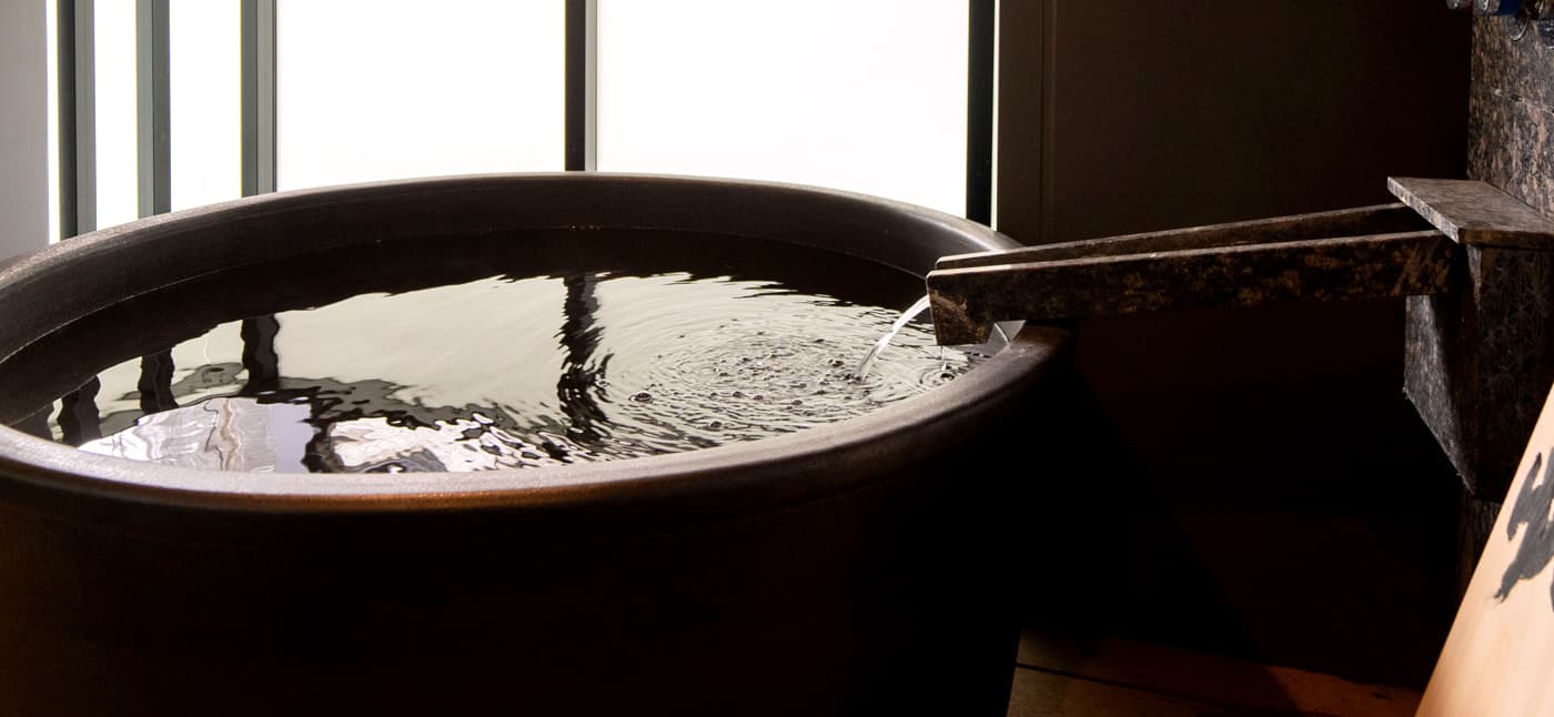 Yubatake Sensui private in-room bath, a deep round black tub being filled by a stone channel spout in front of a frosted window