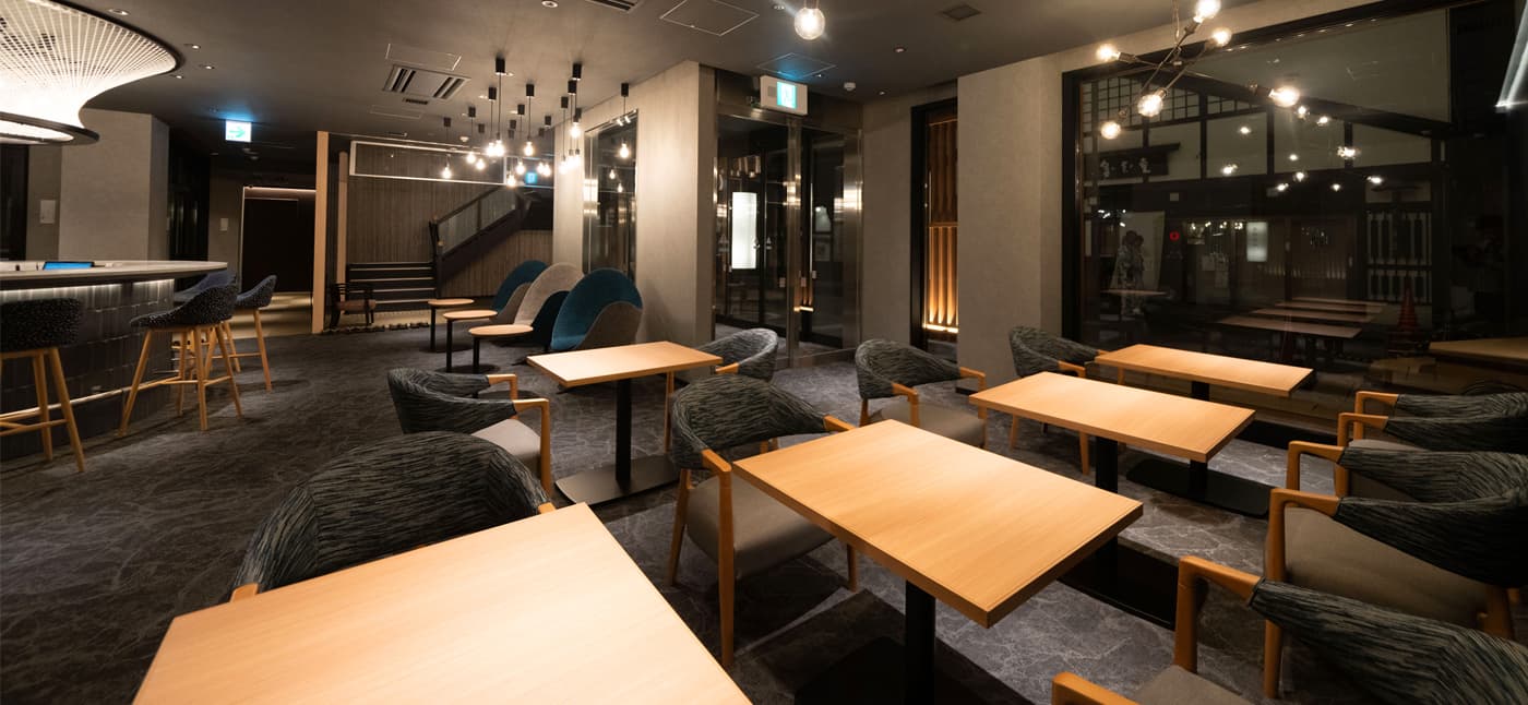 Yubatake Sensui guest lounge with low tables, teal and grey armchairs and pendant lighting beside a slate-tiled bar counter