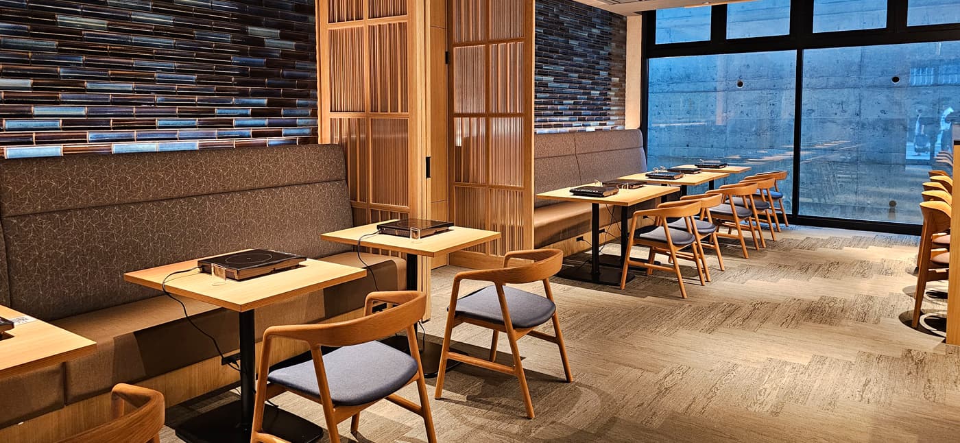 Yubatake Sensui restaurant dining area with wood tables, woven-back chairs and a brick mosaic feature wall by a window