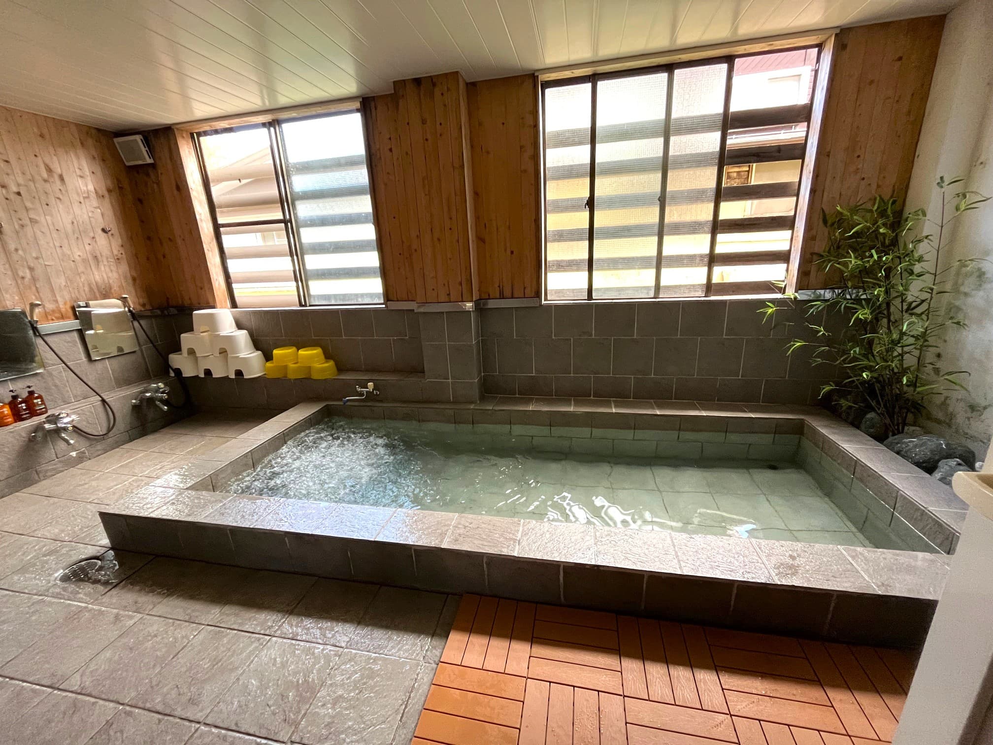 Indoor stone-tiled communal bath with garden-view windows at Matsunoki-tei in Hakuba