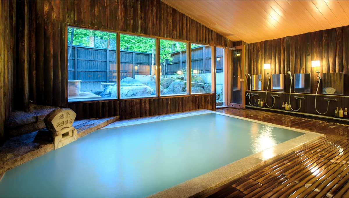 Indoor wood-paneled public bath at Meitoya So filled with milky Zao Onsen sulfur water beside a garden window