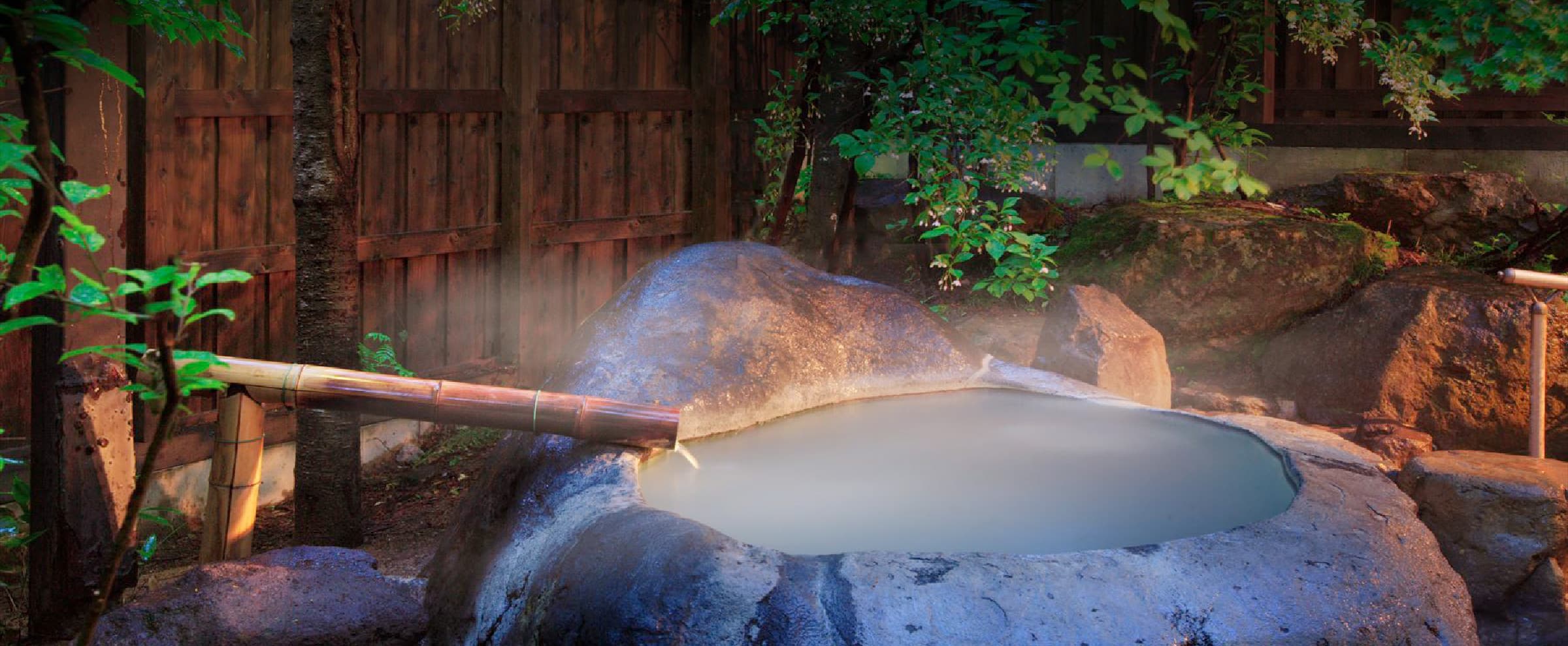 Private open-air stone rotenburo with steaming Zao Onsen sulfur water and a bamboo spout among greenery