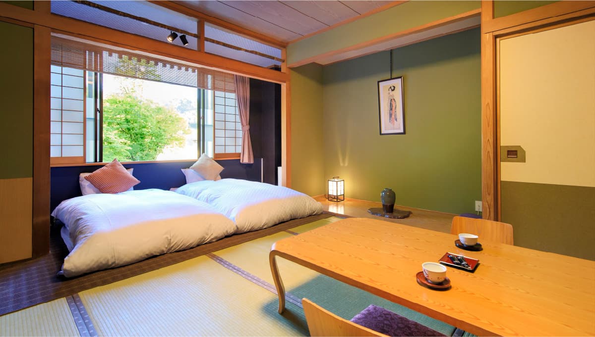 Japanese-style guest room with twin low beds on tatami, a wooden table and garden view at Meitoya So