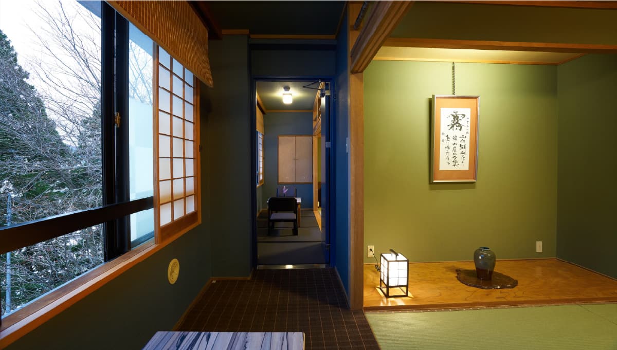 Tatami guest room with a tokonoma alcove, hanging scroll and shoji window overlooking a snowy forest